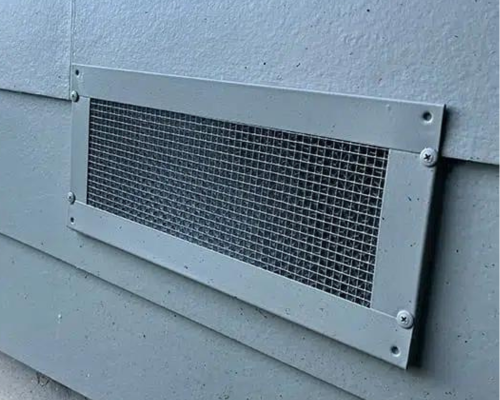 A metal mesh screen mounted on a light gray wall to block embers while allowing airflow.