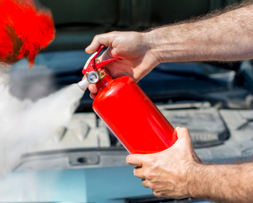 Red fire extinguisher in use, ejecting white powder and red mist over an open engine bay.