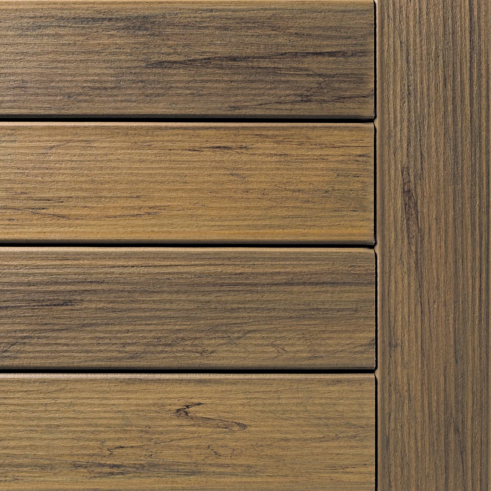 Close-up of Legacy Tigerwood composite decking panels with a vertical trim piece, showing varied wood-grain textures and warm brown tones.