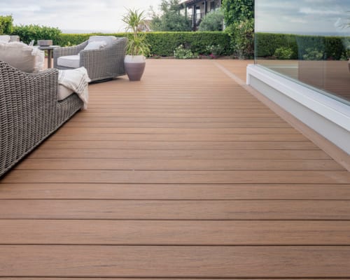 Fire-resistant decking planks laid in a modern outdoor patio with wicker furniture.